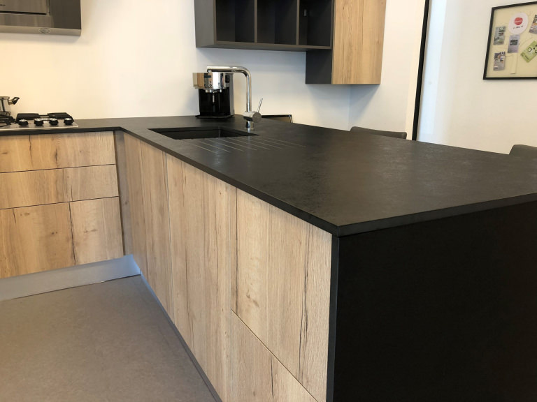 Cuisine en bois clair avec plan de travail noir mat, évier intégré, robinet inox et agencement en L pour un style moderne et épuré. © Fidelem