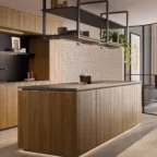 Cuisine contemporaine présentant un grand îlot central en bois, des étagères métalliques suspendues avec éclairage intégré et des éléments décoratifs, dans un espace lumineux et épuré