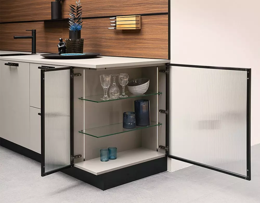 Cuisine moderne avec placard d’angle en verre, portes ouvertes, étagères en verre et vaisselle élégante, design contemporain avec finition bois et blanc, idéale pour rangement et décoration.