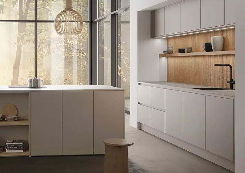 Cuisine contemporaine aux façades blanches mates, grande fenêtre, étagères décoratives et crédence en bois clair, offrant un espace lumineux et épuré.