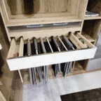 Tiroir ouvert dans un dressing en bois clair, présentant un système de rangement pour pantalons suspendus et des compartiments latéraux pour ceintures ou accessoires.