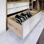 Tiroir coulissant bas dans un dressing en bois clair, spécialement conçu pour organiser et ranger des paires de chaussures, dont des baskets noires et grises.