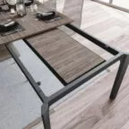 Vue rapprochée d’une table à manger extensible en bois et métal, montrant le mécanisme d’extension avec une rallonge centrale partiellement installée.