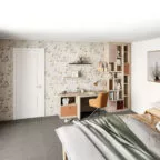 Chambre lumineuse pour enfant ou adolescent, avec un papier peint floral, un bureau d’angle en bois clair, une chaise orange et des étagères verticales pour livres et objets décoratifs.