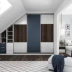 Placard dressing moderne aménagé sous une pente de toit, avec portes coulissantes, tiroirs intégrés, étagères ouvertes et finitions bois et bleu, dans une chambre lumineuse avec parquet foncé et tapis à motifs.