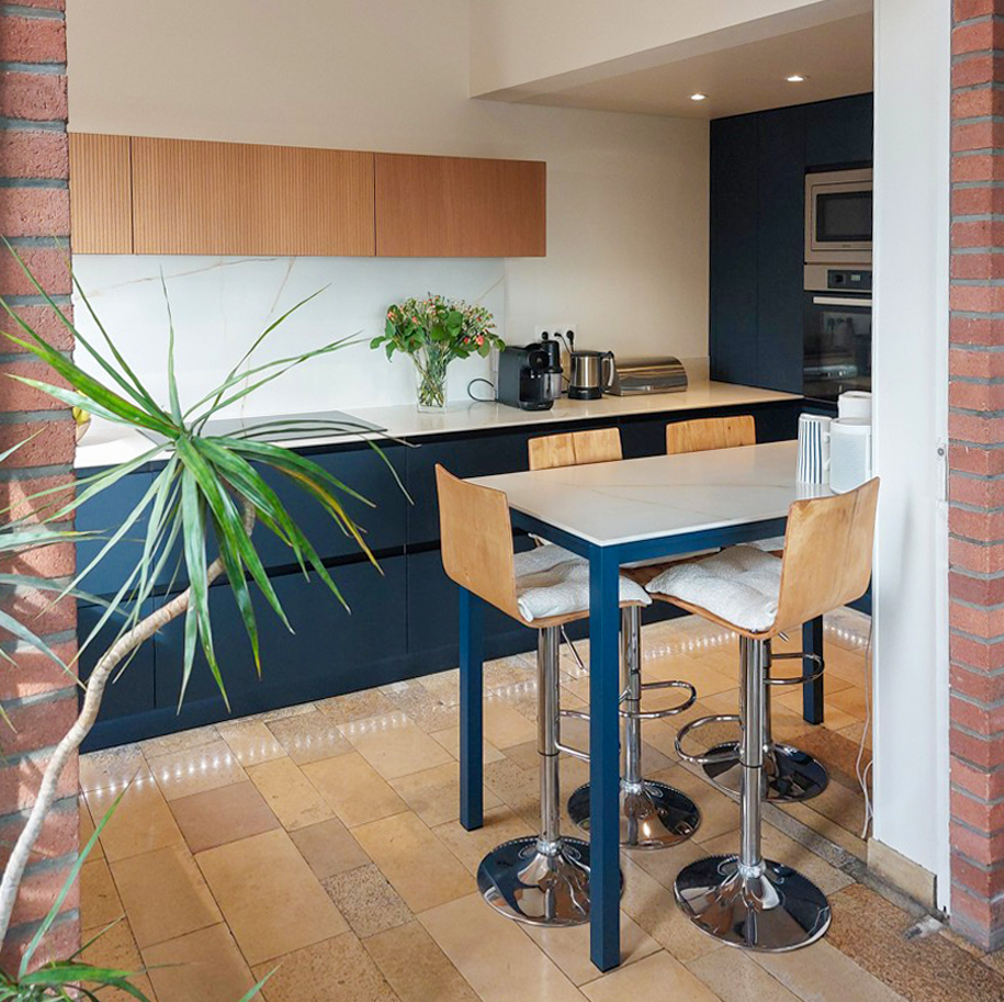 Espace repas intégré avec table haute et chaises design, au cœur d’une cuisine sur mesure moderne signée Cuisines Premier Plan Le Havre, ambiance chaleureuse et contemporaine.
