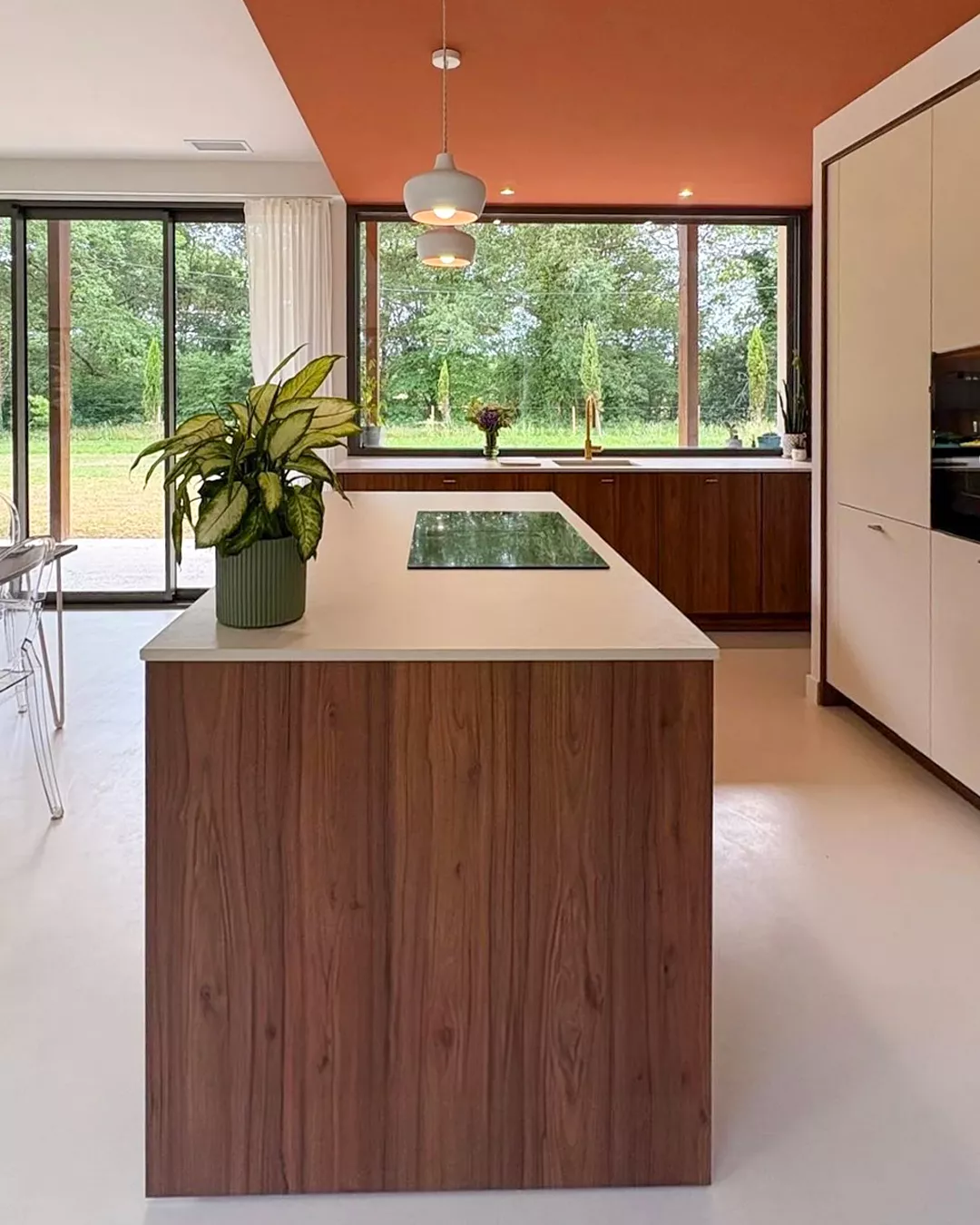 Cuisine ouverte sur l’extérieur avec grand îlot, plan de cuisson intégré, mobilier bois noyer et plafond terracotta, conçue par Premier Plan Anglet