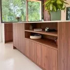 Îlot central en bois noyer avec rangements ouverts, plan de travail clair et accessoires déco, dans une cuisine sur mesure lumineuse signée Premier Plan Anglet