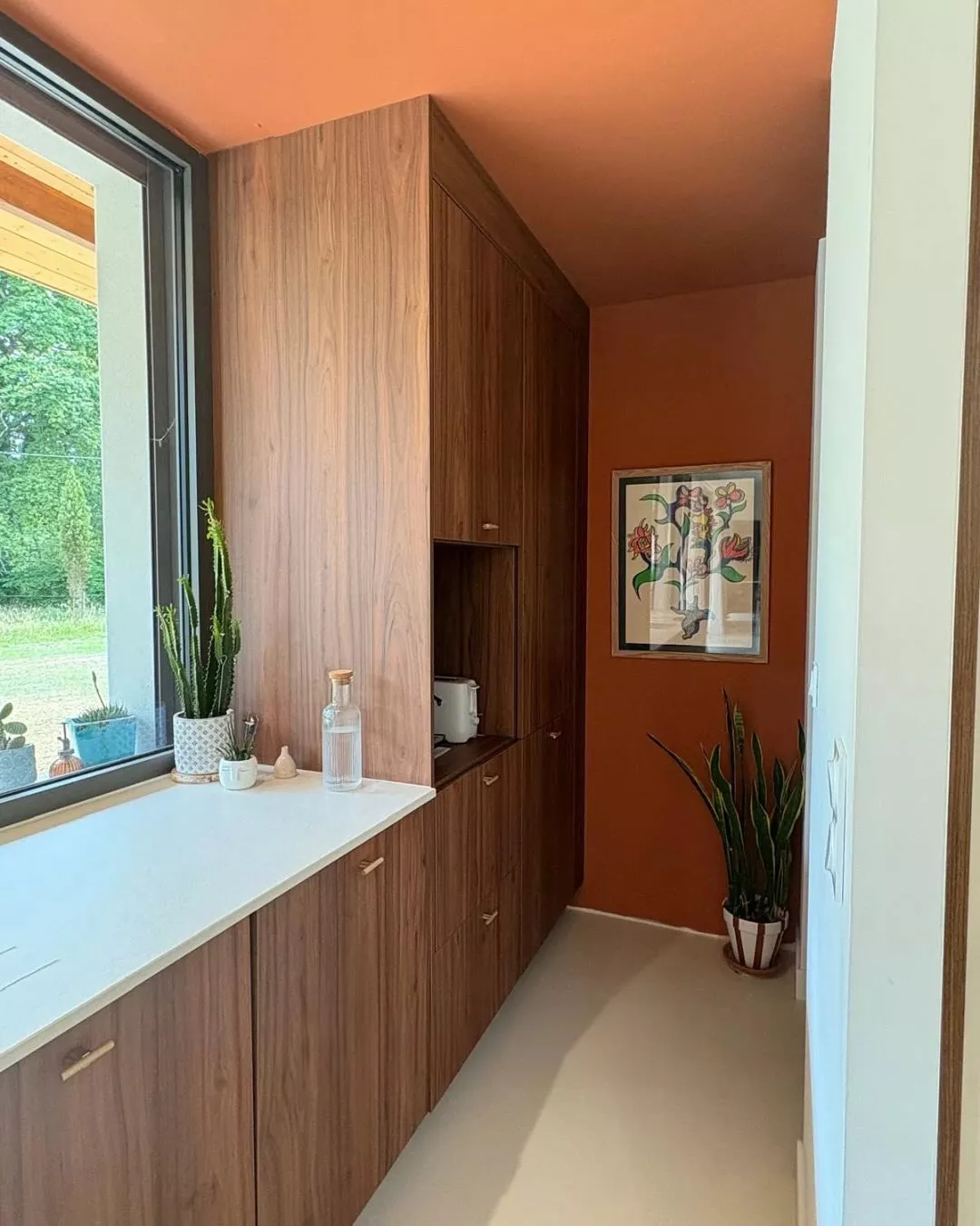 Couloir de cuisine avec meubles hauts en bois, plan clair et mur terracotta, avec des plantes et une illustration murale, projet sur mesure Premier Plan Anglet