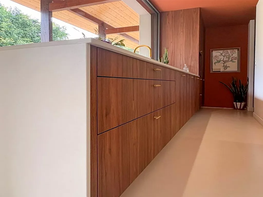 Enfilade de tiroirs en bois noyer avec poignées dorées, plan de travail clair avec rigoles d’égouttage, cuisine haut de gamme Premier Plan Anglet