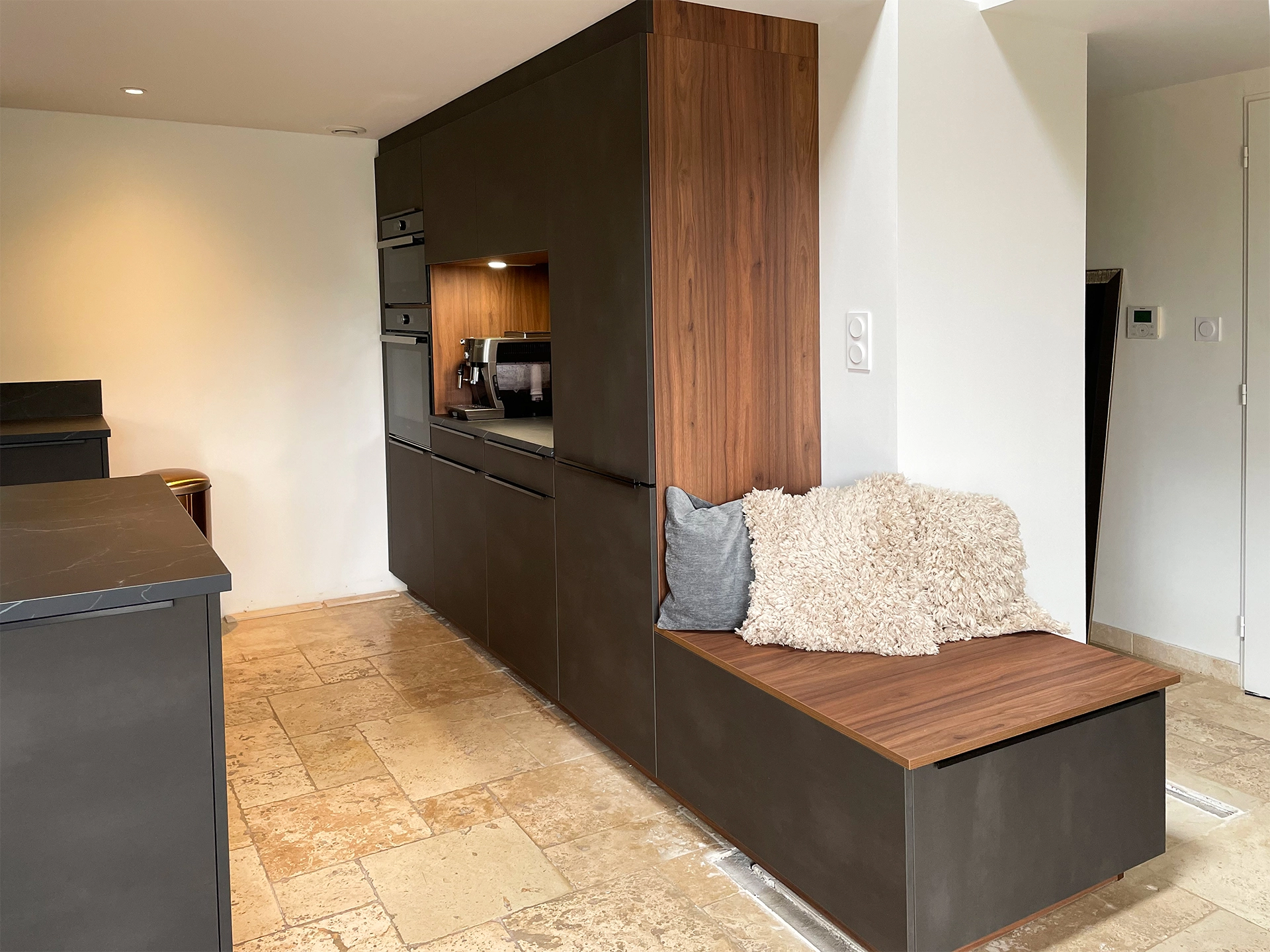 Découvrez l’intégration astucieuse d’une banquette avec rangements sur mesure, combinée à des meubles de cuisine modernes en finition sombre et noyer, parfaitement adaptée à l’espace sous mezzanine au Bois d’Oingt. Cette réalisation optimise chaque centimètre pour une circulation fluide et un accueil chaleureux.