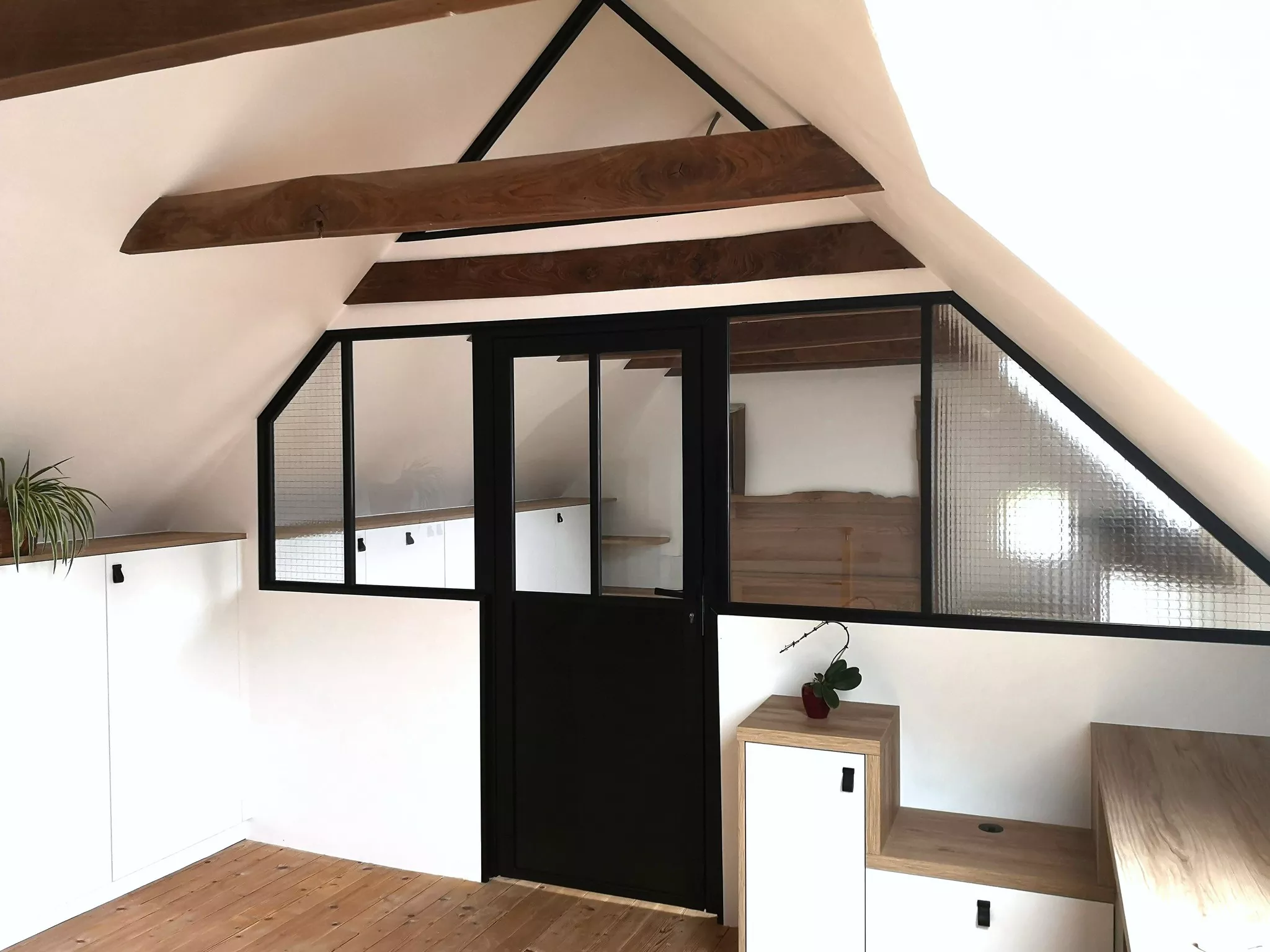 Vue d’ensemble d’un aménagement de mezzanine sur mesure signé Premier Plan Pont-l’Abbé, avec verrière noire, poutres apparentes et meubles en blanc et chêne clair pour un rendu lumineux et chaleureux.