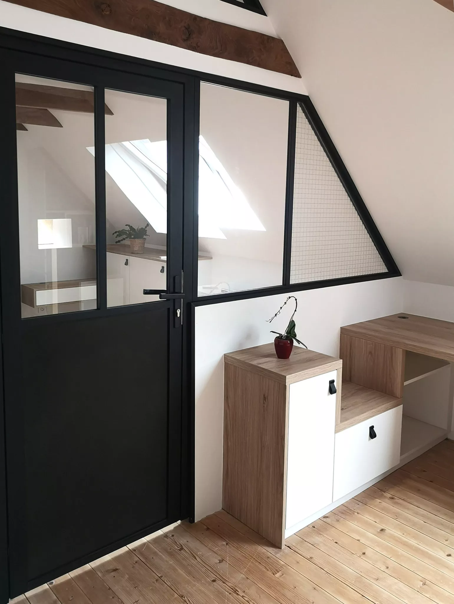 Détail de la verrière noire sur mesure séparant la chambre du coin bureau, intégrée à une mezzanine conçue par Premier Plan Pont-l’Abbé avec mobilier en bois et blanc mat.