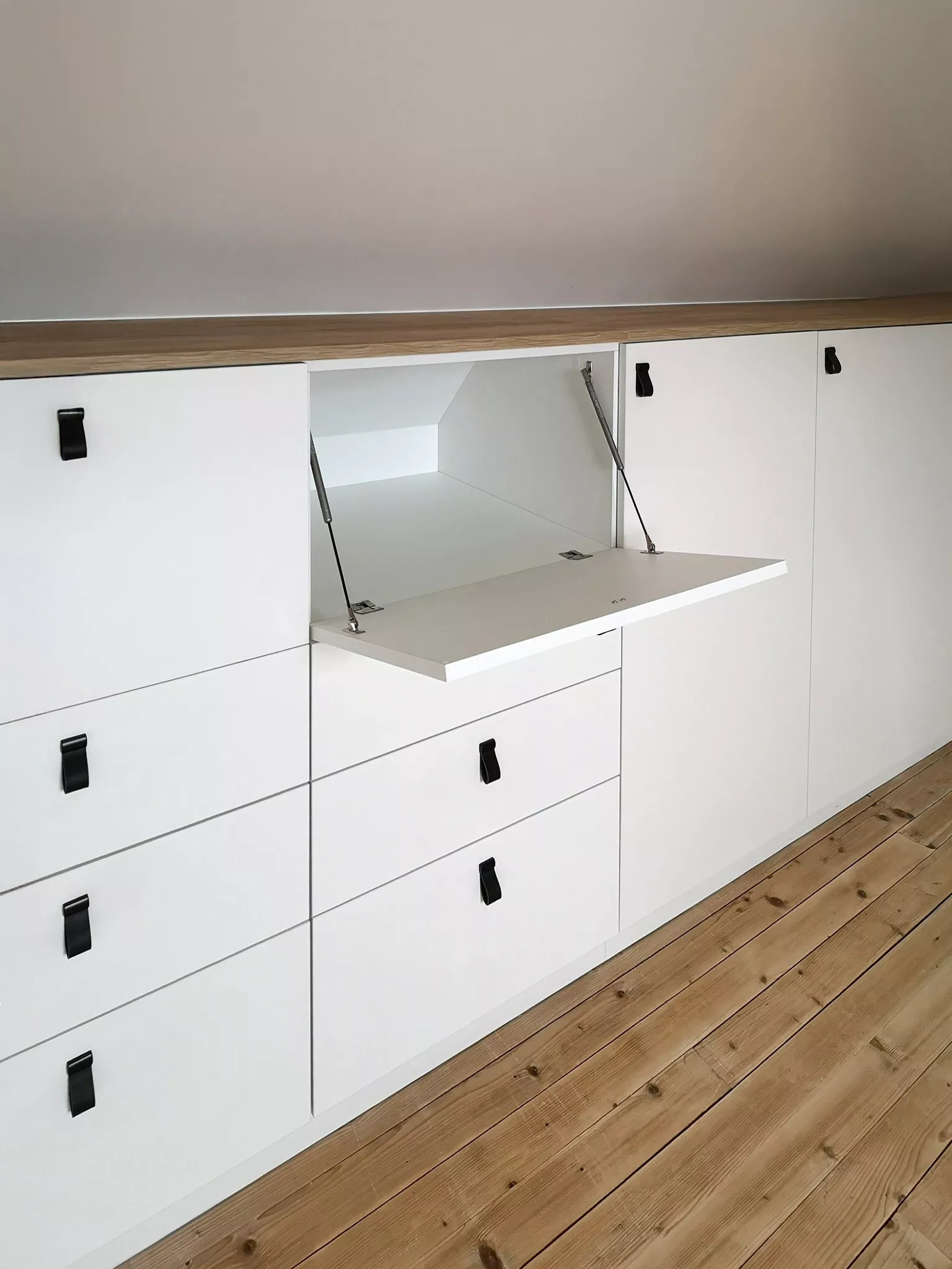 Meuble à abattant intégré dans un aménagement de mezzanine sur mesure, offrant un espace de rangement pratique et discret sous les combles.