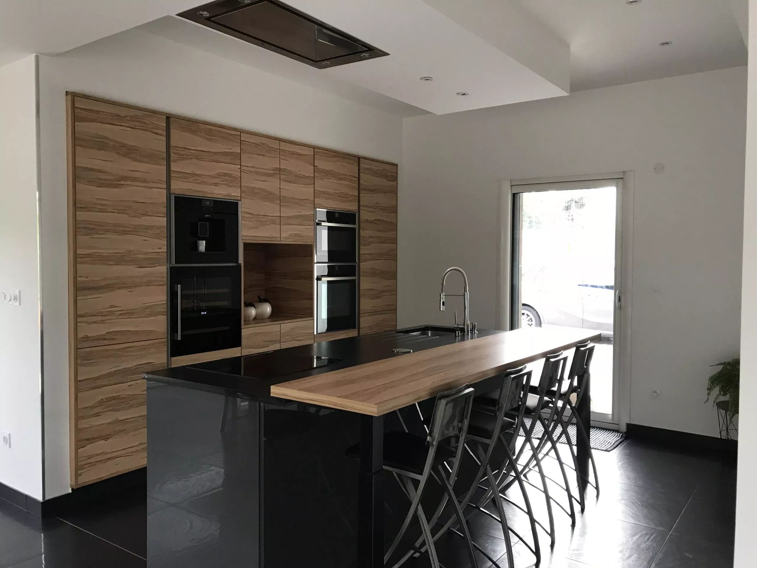 Vue latérale d'un îlot de cuisine avec plan bar en stratifié décor bois de rose et chaises hautes design.