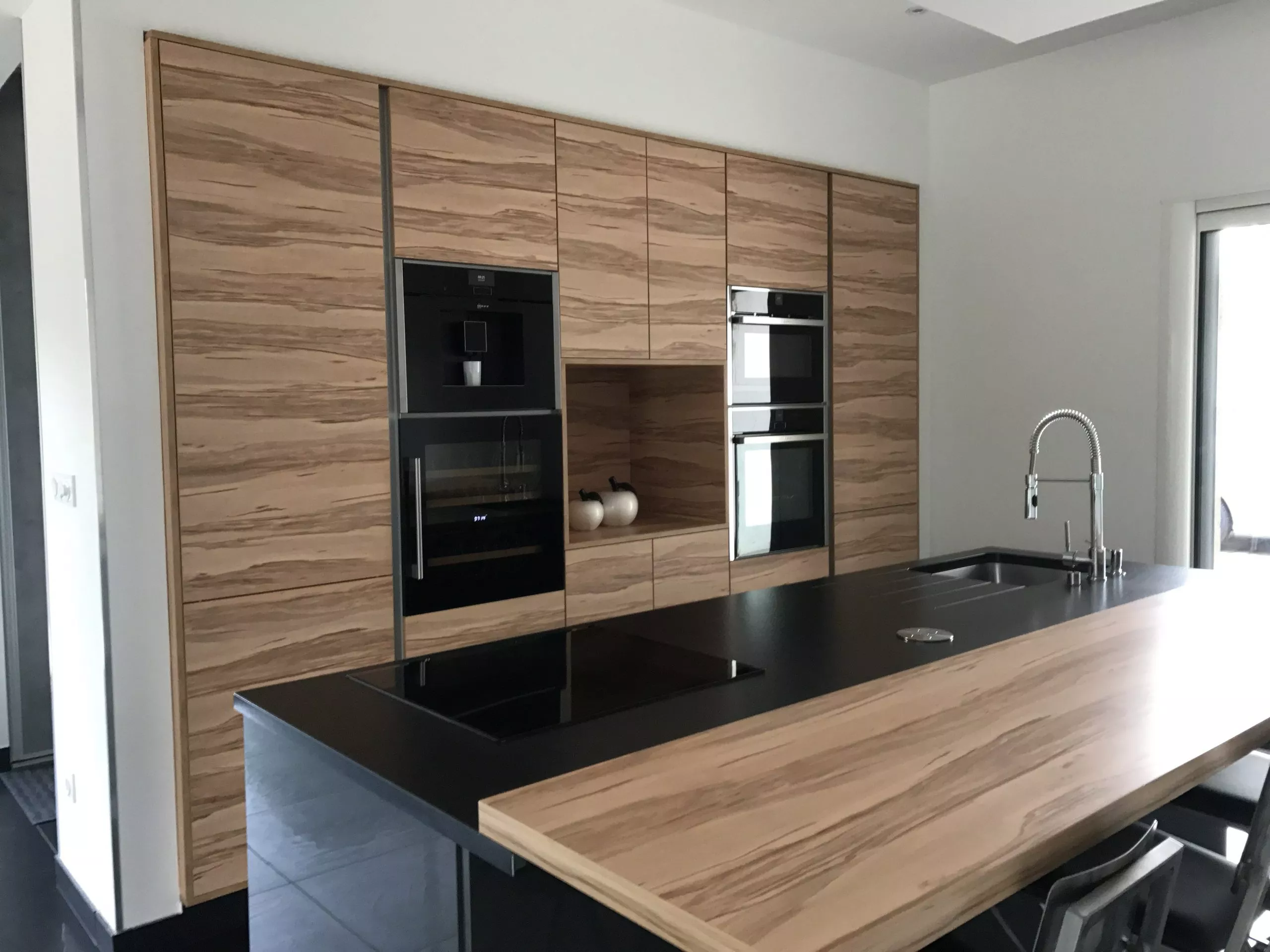 Vue de trois-quarts d'une cuisine équipée avec plan de travail en granit noir et façades texturées bois.