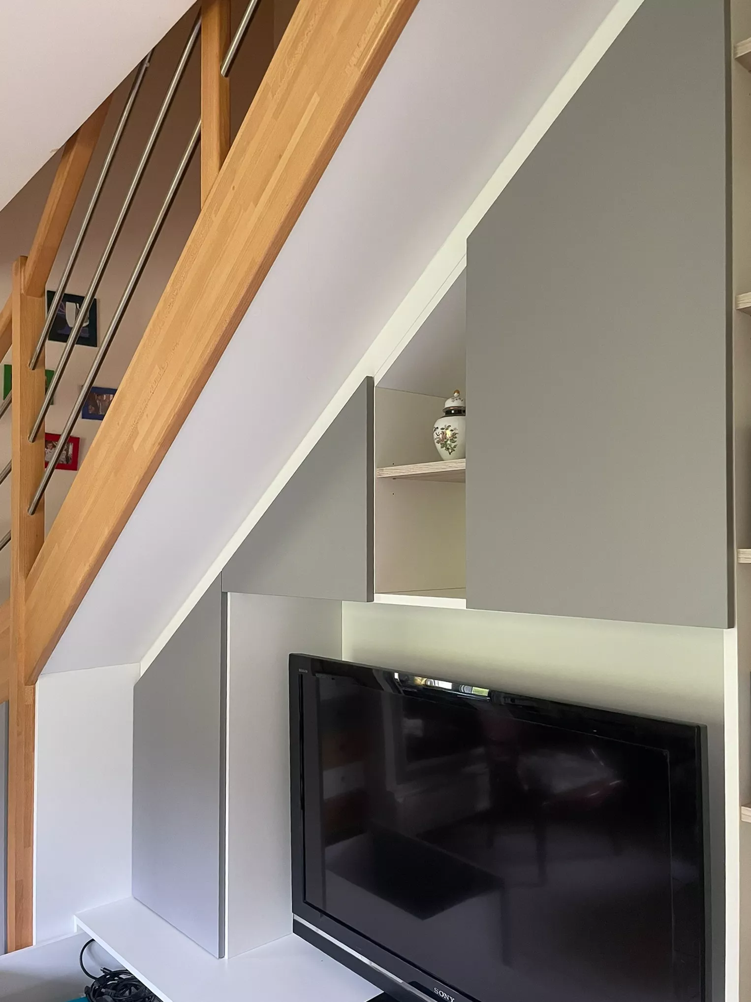 Gros plan sur la finition technique : porte de placard découpée en triangle s'ajustant au millimètre sous la pente de l'escalier en bois.