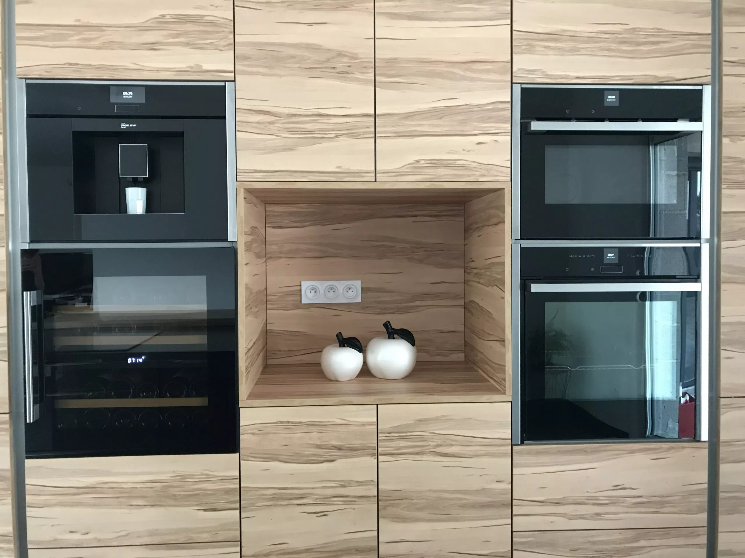 Bloc armoires de cuisine en décor bois intégrant un four, une machine à café et une cave à vin encastrée.