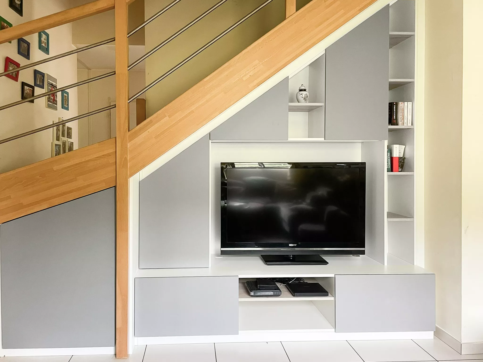Vue globale de l'aménagement Premier Plan Le Bois d'Oingt : meuble TV et zone de stockage contournant un pilier structurel pour optimiser tout le volume sous l'escalier.