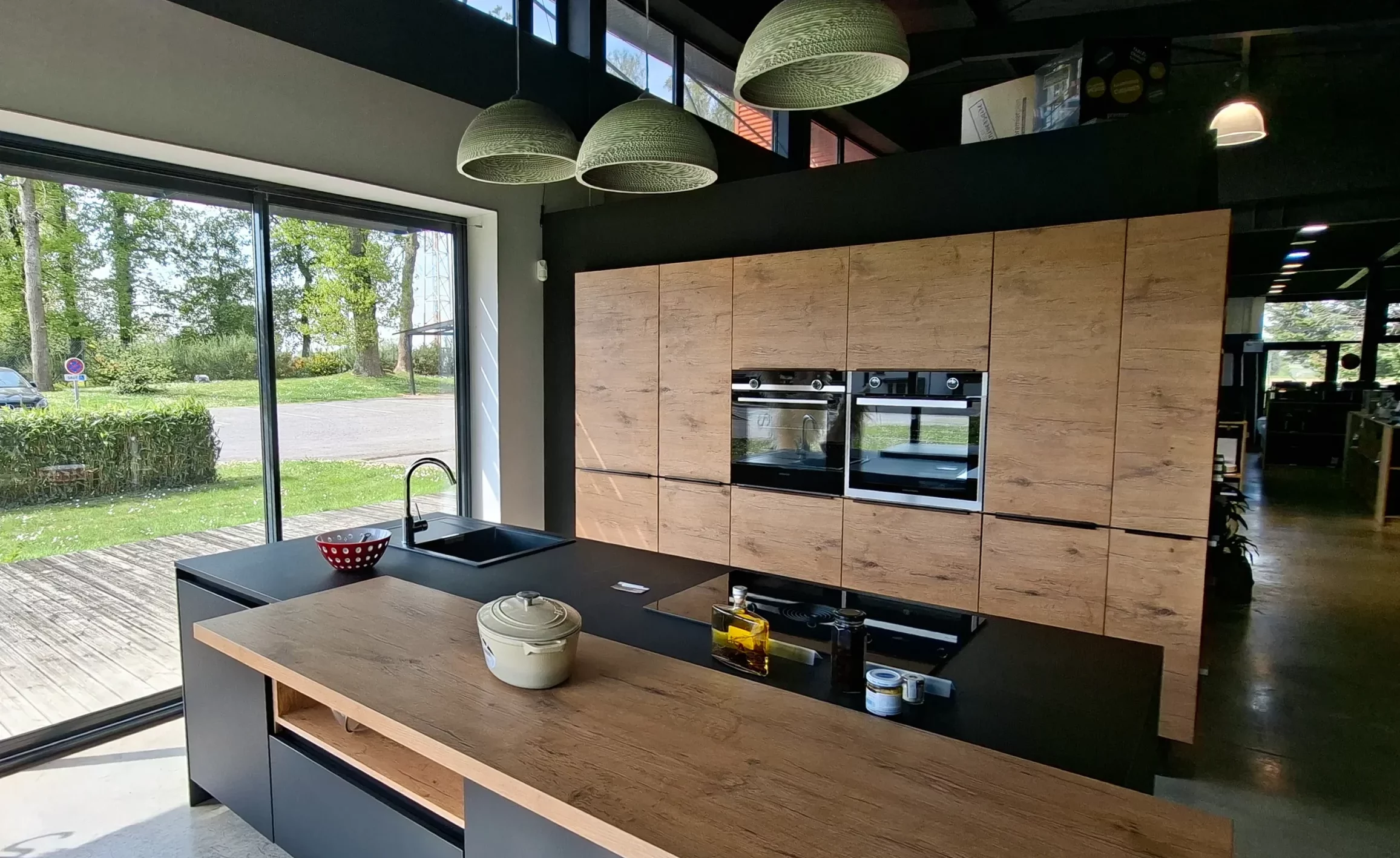 Aménagement de cuisine spacieuse avec un mur de colonnes en bois et un îlot noir mat avec coin repas.