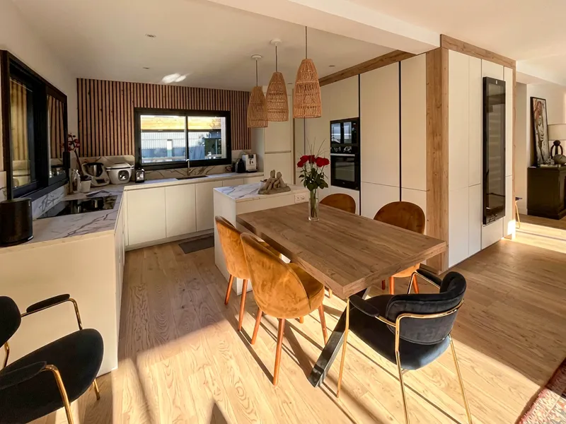 Cuisine sans poignée Premier Plan Fécamp avec façades blanches, décor bois, îlot central et grande table attenante.
