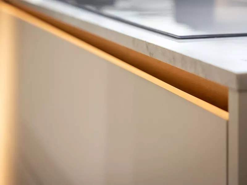Détail d’une cuisine contemporaine avec gorge lumineuse, plan de travail effet pierre et façade claire épurée.