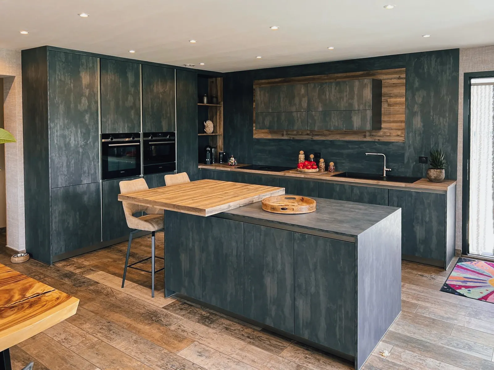Cuisine contemporaine sur mesure avec îlot central, coin repas intégré, façades texturées foncées et décor bois chaleureux.