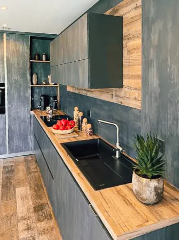 Cuisine Premier Plan Fécamp avec évier noir intégré, plan de travail bois et meubles hauts effet minéral.