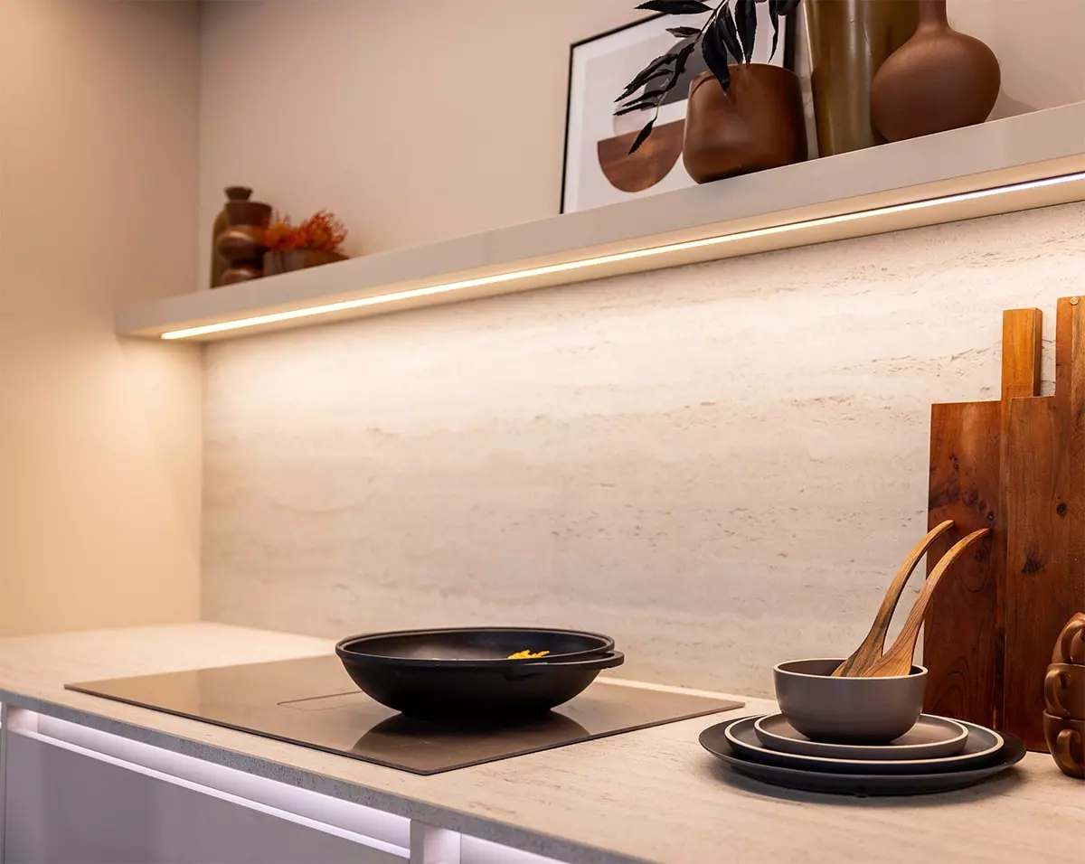 Détail d’une cuisine Rotpunkt avec plan de cuisson intégré, crédence effet pierre claire et étagère lumineuse.