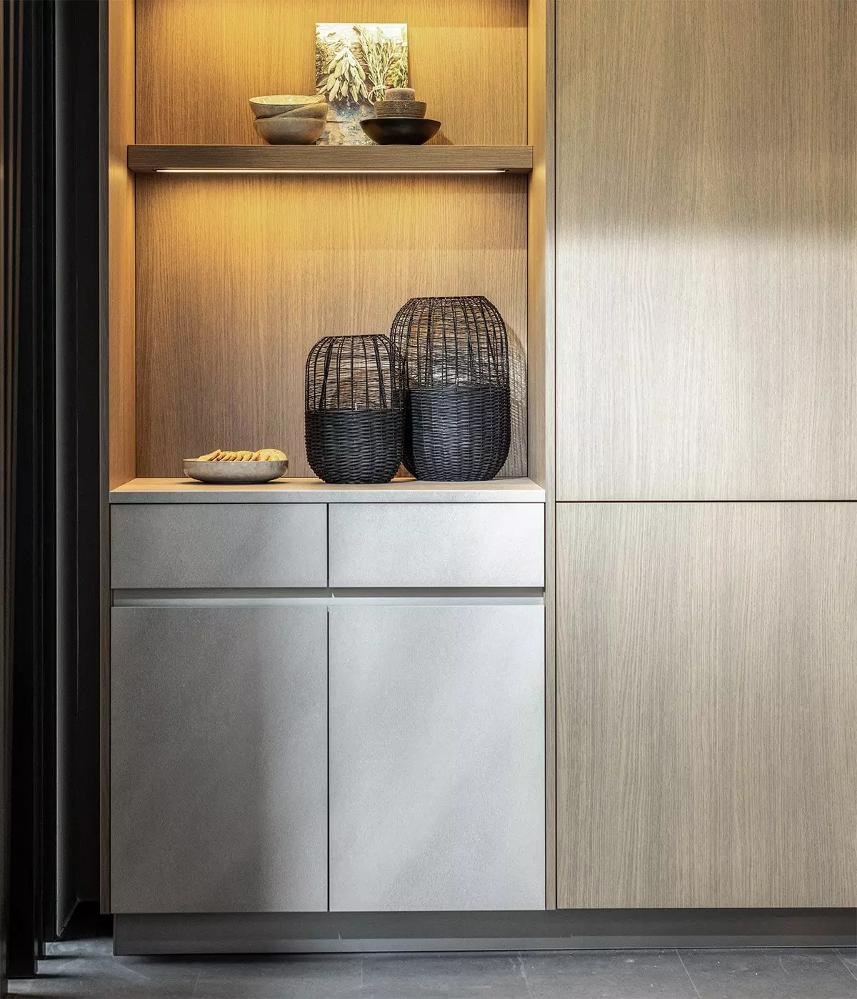 Cuisine Rotpunkt avec niche ouverte éclairée, rangements gris effet pierre et façades bois aux veinages marqués.