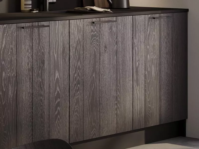 Gros plan sur des façades cuisine à texture bois verticale et finition sombre.