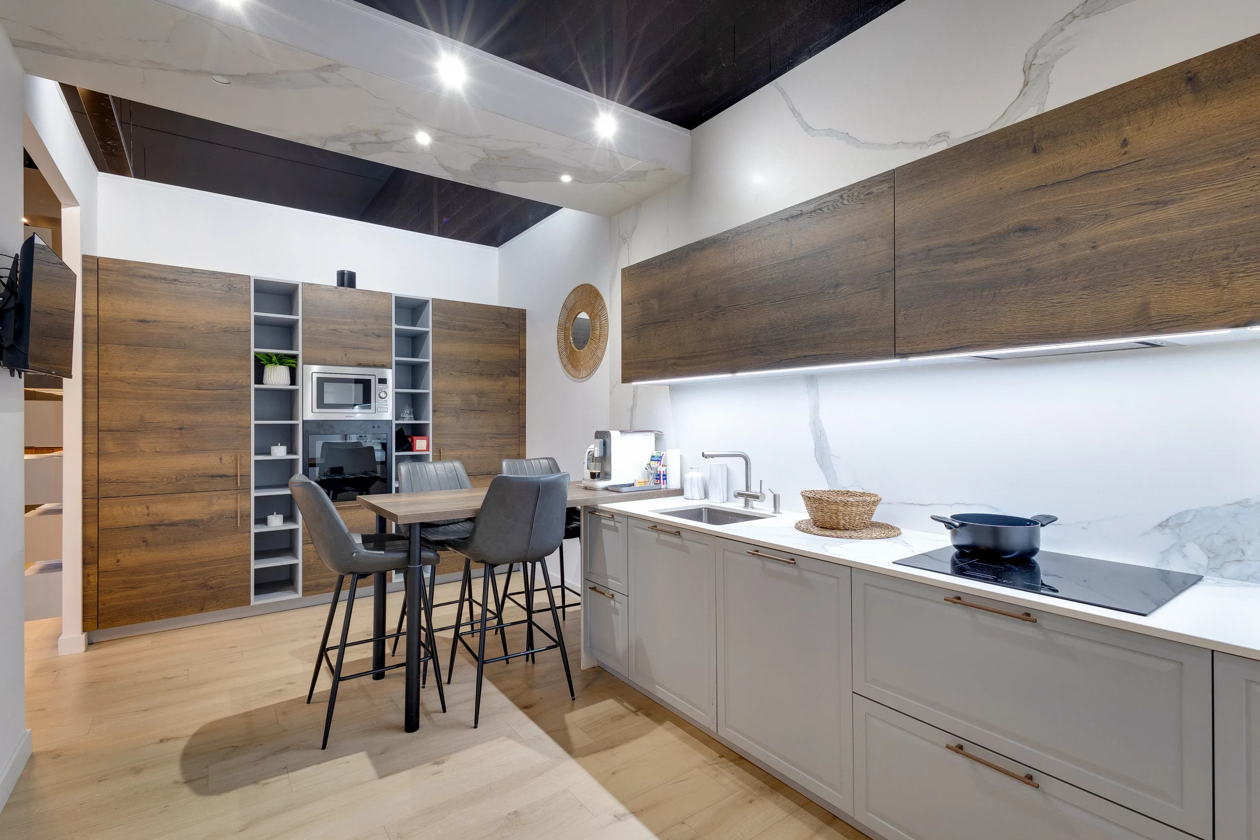 Cuisine d’exposition du showroom Premier Plan Carbonne avec façades bois, meubles bas gris clair, crédence effet marbre et espace repas intégré.