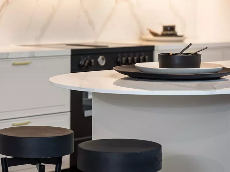 Ilot central effet marbre blanc, crédence blanche et tabouret dans une cuisine Rotpunkt.