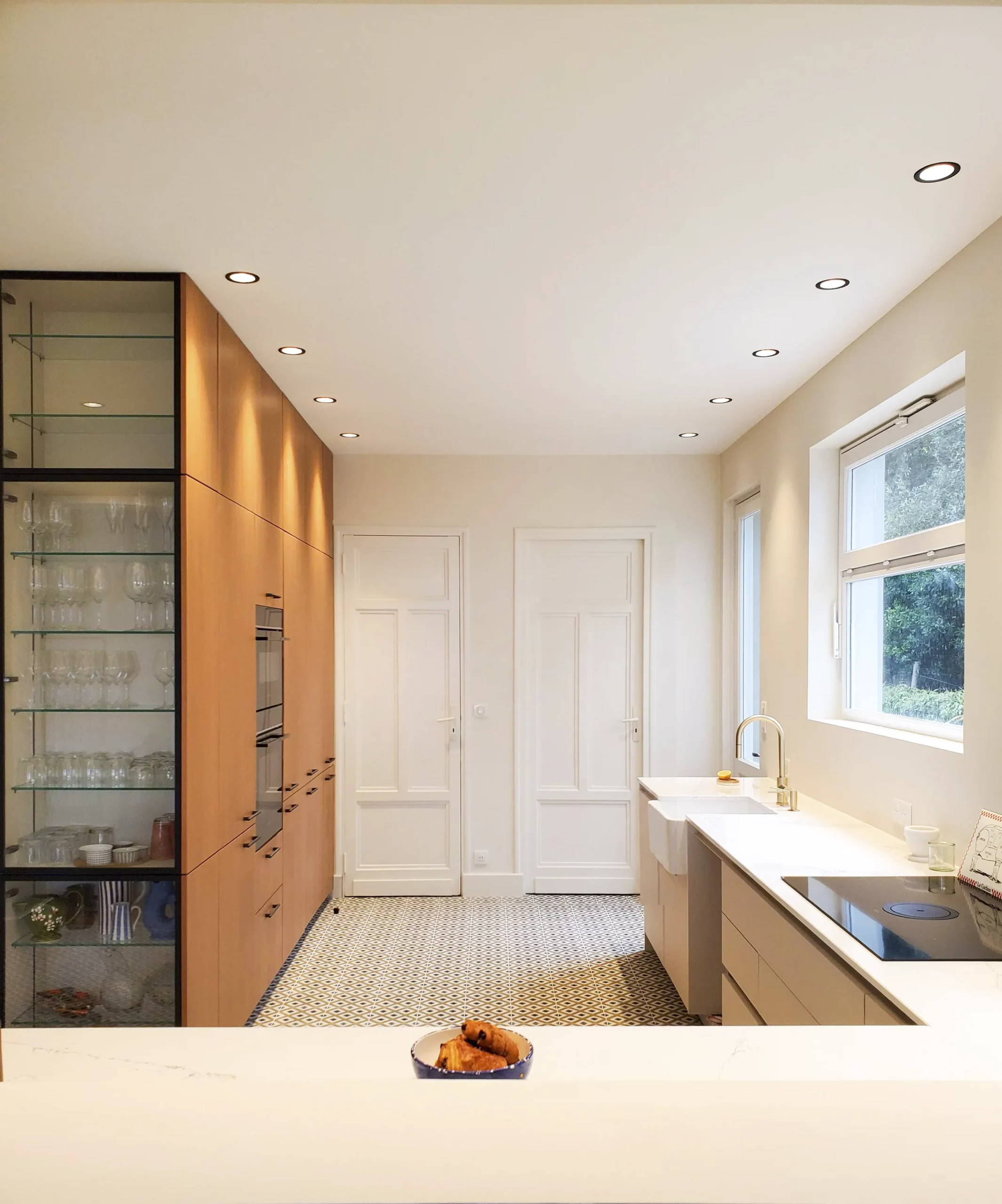 Cuisine sur-mesure Premier Plan Montauban avec colonnes en bois, vitrine noire, plan de travail clair et sol à motifs graphiques