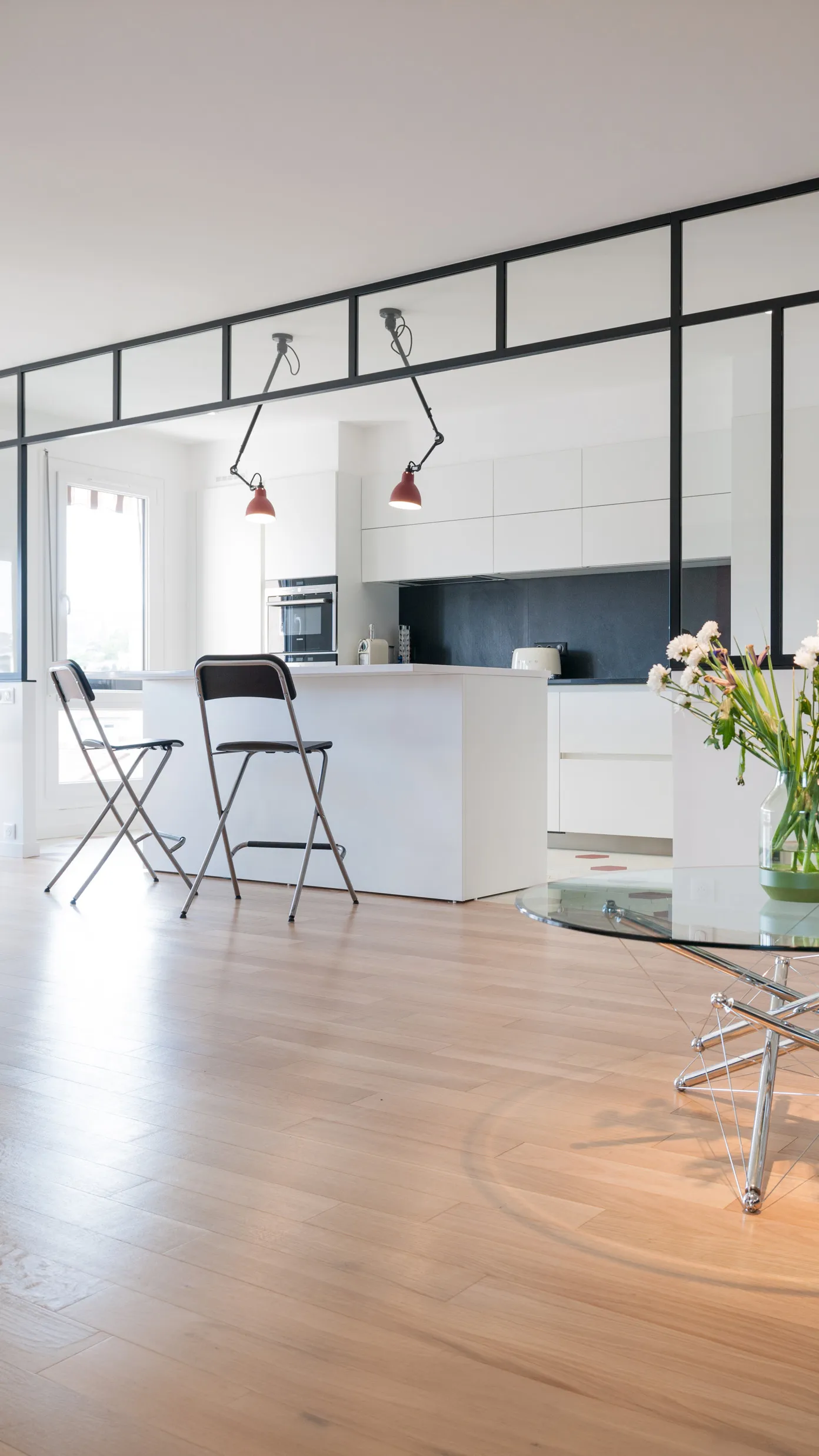Cuisine sur mesure tout blanc avec îlot central, crédence noire, verrière d'atelier et luminaires rouges orientables, sol en parquet clair, réalisée par Cuisines Premier Plan à Cournon-d'Auvergne