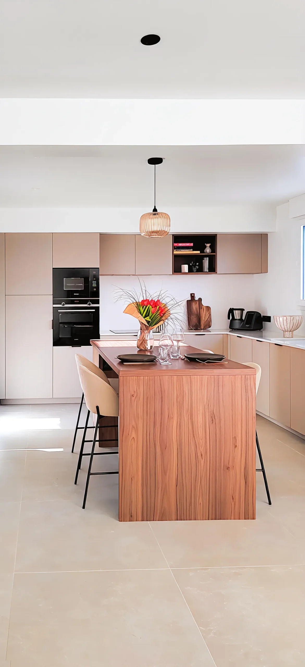 Cuisine sur mesure avec façades rose-nude mate, îlot central habillé bois de noyer avec plan de travail assorti, suspension en rotin ajouré et électroménager noir encastré, réalisée par Cuisines Premier Plan à Locminé