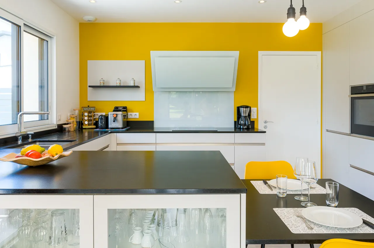 Cuisine en L Premier Plan Pont-l’Abbé avec façades blanches, plan de travail noir, mur jaune et espace repas attenant