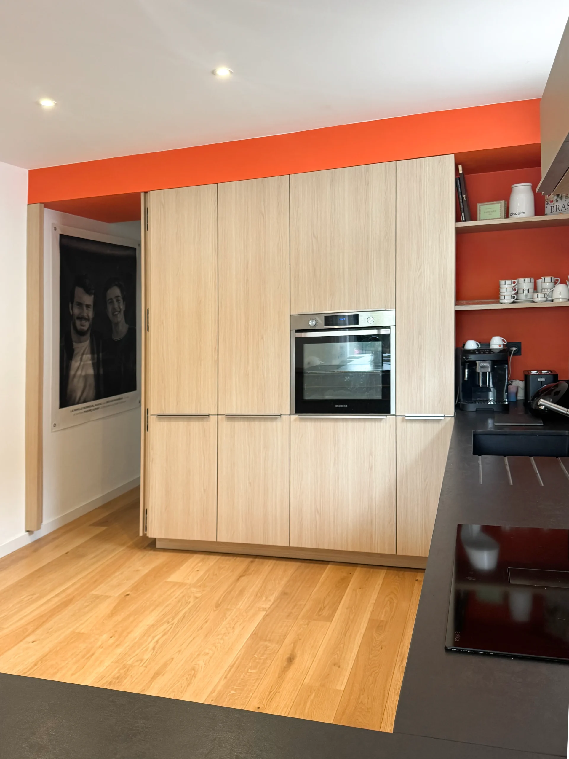 Cuisine sur-mesure Premier Plan Carbonne avec porte dérobée dissimulée dans un mur de colonnes en bois clair, four encastré et niches ouvertes sur fond terracotta
